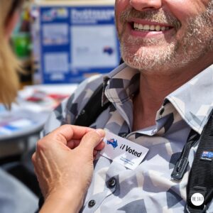 Close-up of 'I Voted' sticker being placed on shirt of person with visible disability, proud expression, Australian electoral materials in background, bright natural lighting, empowering moment