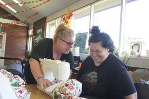 NDIS support worker supporting a participant during a sewing activity at a SALT Foundation community hub.